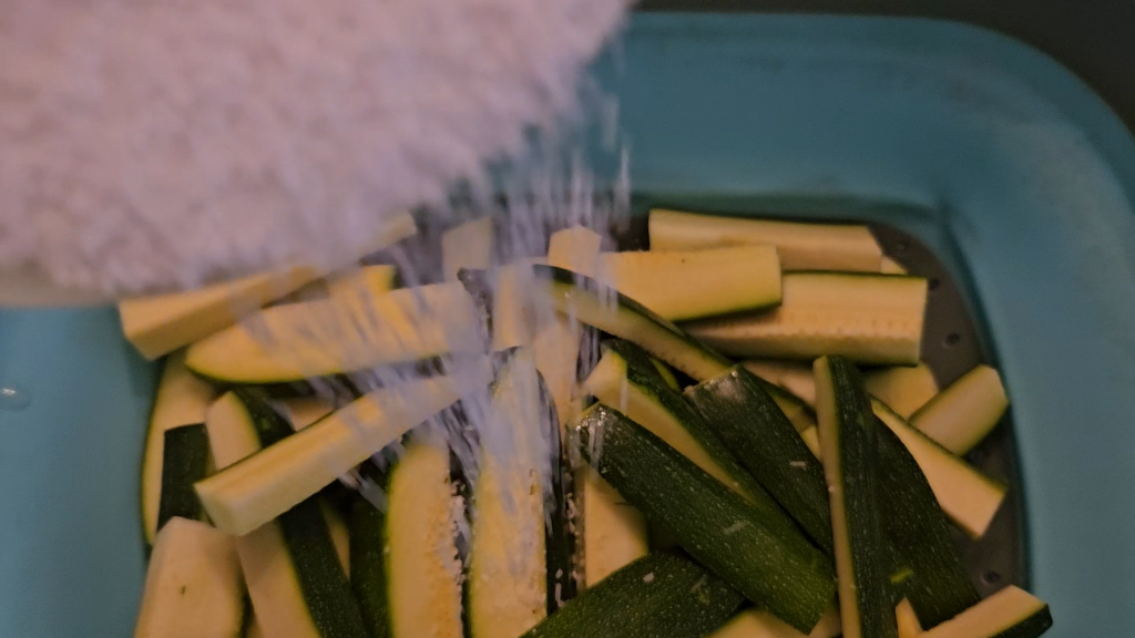 Pouring salt onto zucchini. The salt helps the zucchini sweat, which makes it stay more crispy in the freezer.