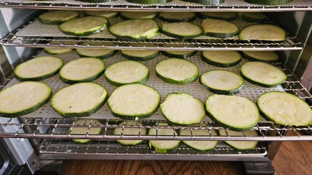 Cosori dehydrator with trays of sliced zucchini, some trays pulled out for visibility.