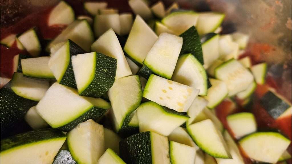 cubed zucchini on top of tomato sauce and spices in a pot.