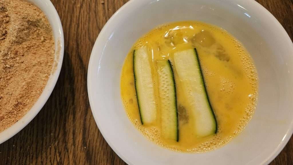 Zucchini spears in beaten eggs before breading.