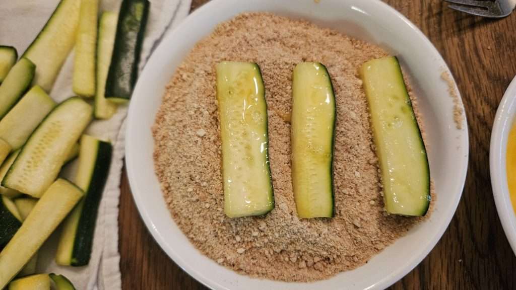 Zucchini that has been dipped in eggs sitting in a bowl of breadcrumbs.