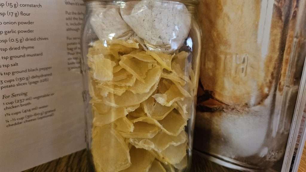 A mason jar filled with dehydrated sliced potatoes with a zippered bag with the scalloped potatoes sauce ingredients on top.