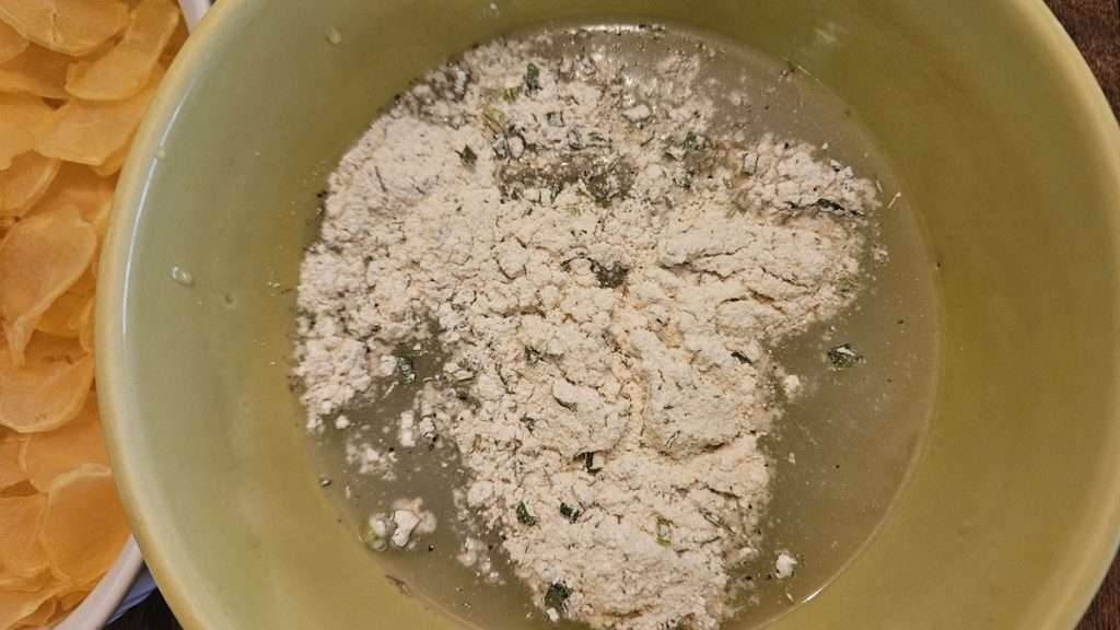 The mixing bowl with water with the scalloped potatoes sauce mixture dumped on top.