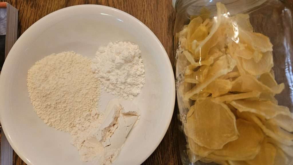 This photo is a close up of a bowl with powdered milk, cornstarch and flour, and a jar with dehydrated sliced potatoes.