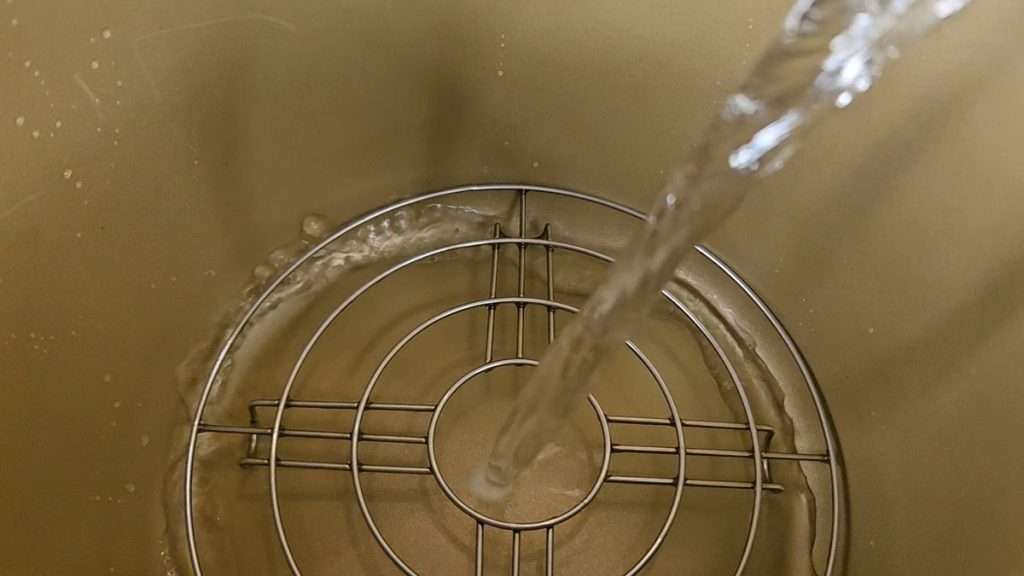 Hot water being poured into Nesco canner to prepare for steaming.