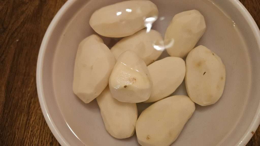 Bowl of peeled russet potatoes submerged in water.