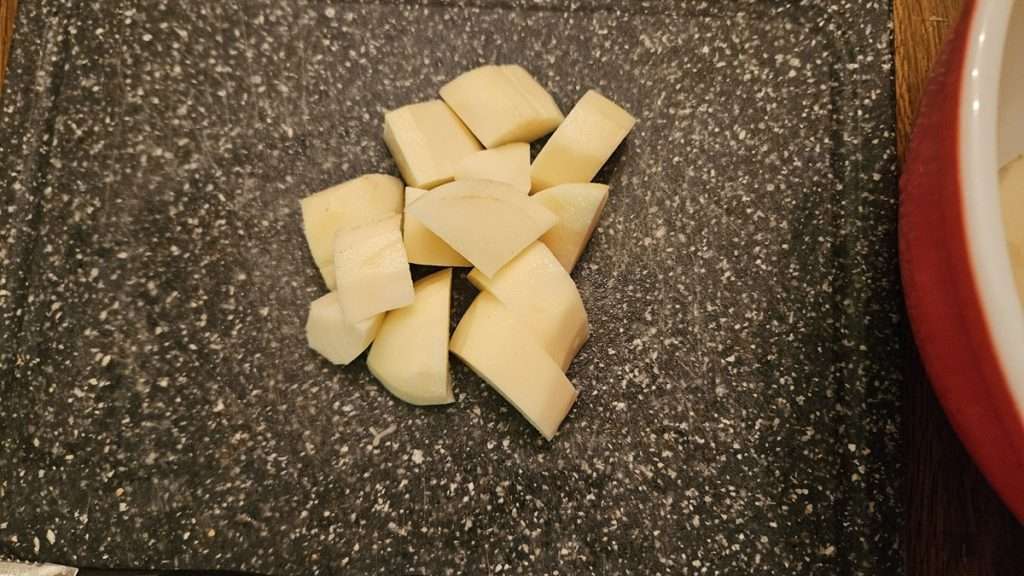 One russet potato cut into cubes on a cutting board.
