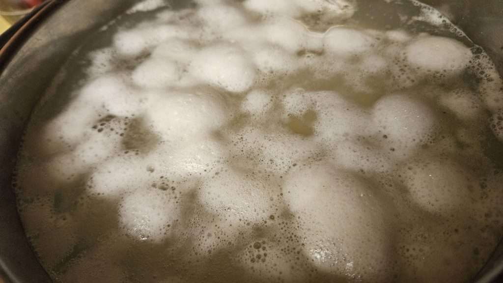 Potatoes boiling in a pot with foam on top of water.