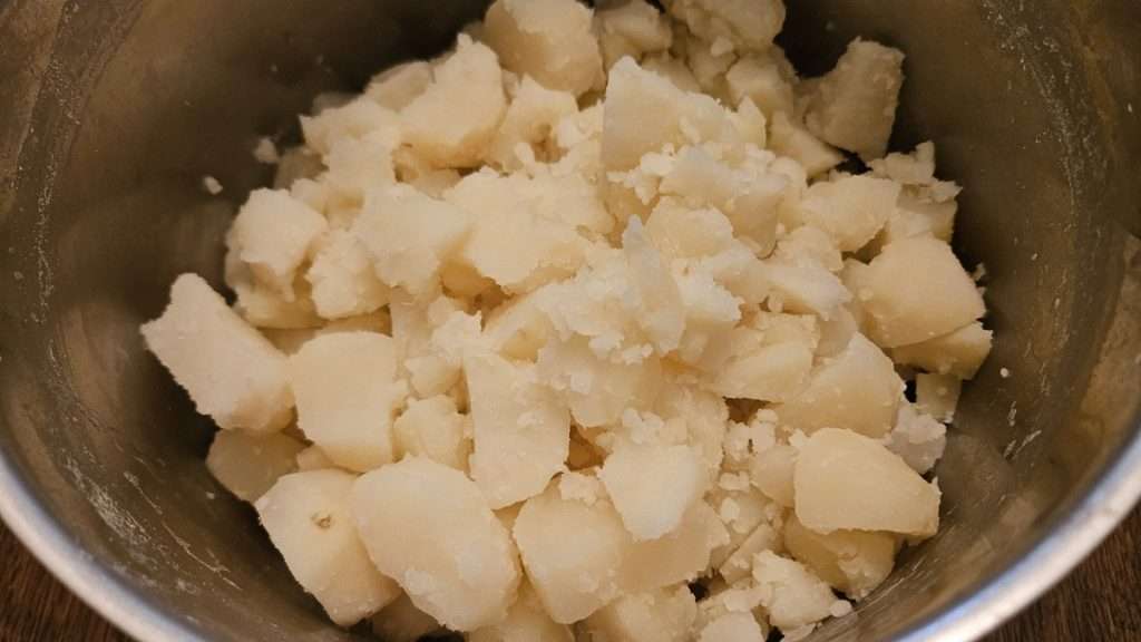 Soft boiled potatoes in a stainless steel pot after draining, ready to mash.