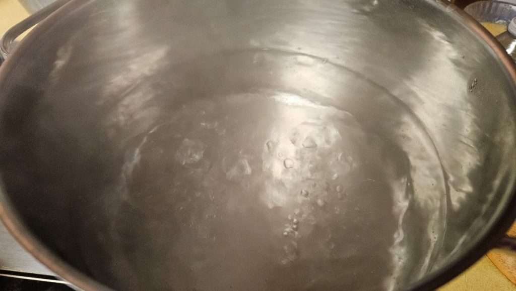 Stainless steel pot of water heating on the stove for cooking sweet potatoes
