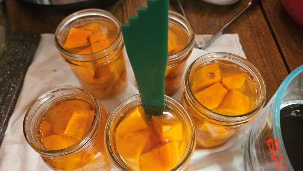 Debubbling tool inserted into jar of hot sweet potatoes and water