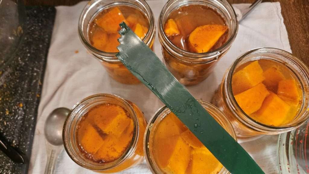 Headspace and debubbling tool laid across jars of sweet potatoes