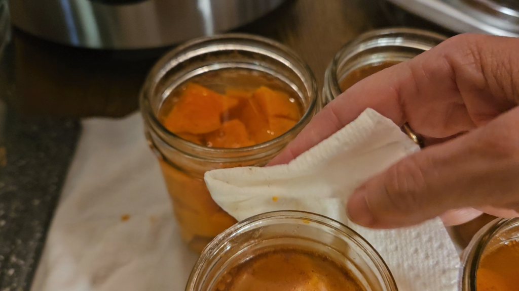 Paper towel dipped in vinegar wiping the rim of a filled sweet potato jar