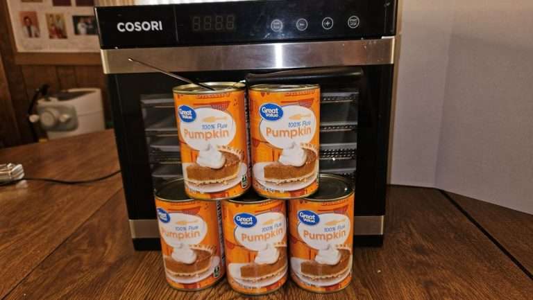 Five cans of pumpkin puree arranged in front of a stainless steel Cosori dehydrator.