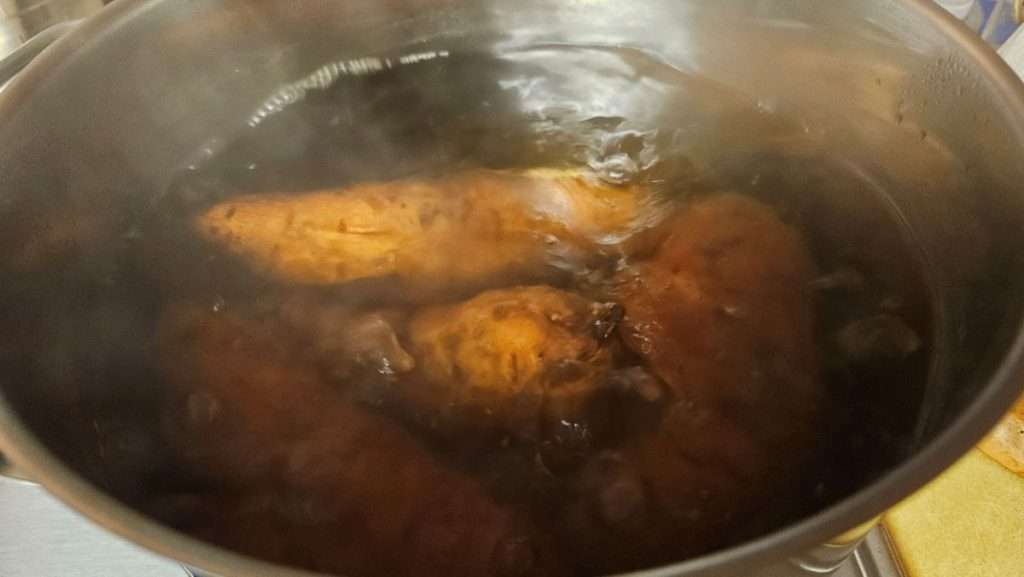 Raw sweet potatoes boiling in a large pot of water