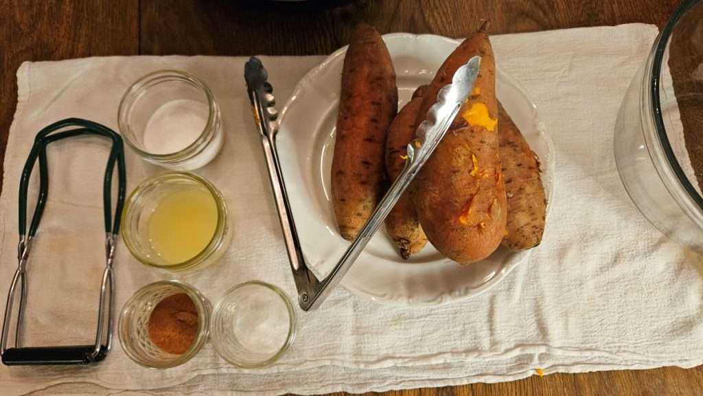 Canning tools and ingredients arranged on a towel with cooked sweet potatoes on a plate