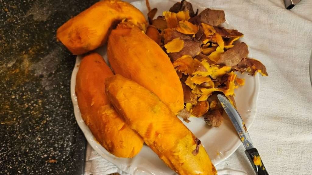Peeled partially cooked sweet potatoes on a plate with removed peels beside them